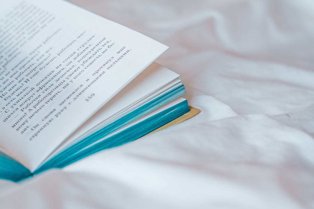 Close-up of an open book on white fabric, featuring turquoise edges. Ideal for education or literature themes.